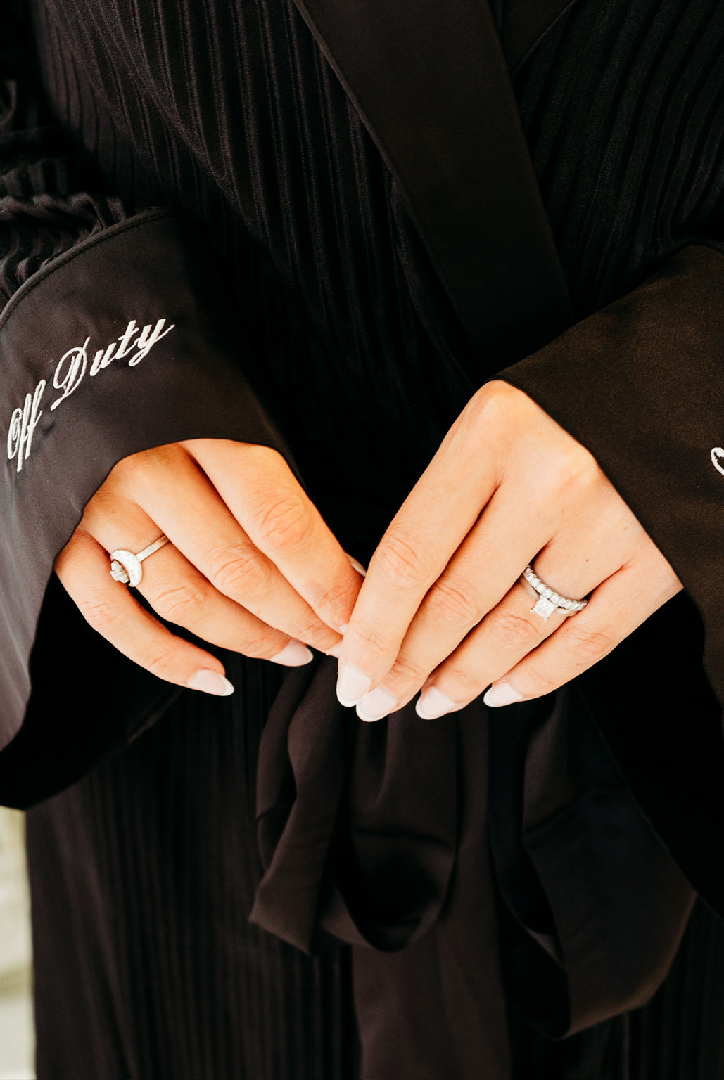 A close-up of a person wearing a black pleated robe with wide cuffs. The left cuff has the words 'Off Duty' embroidered in white script, and the right cuff has 'Ghster' embroidered in white script.