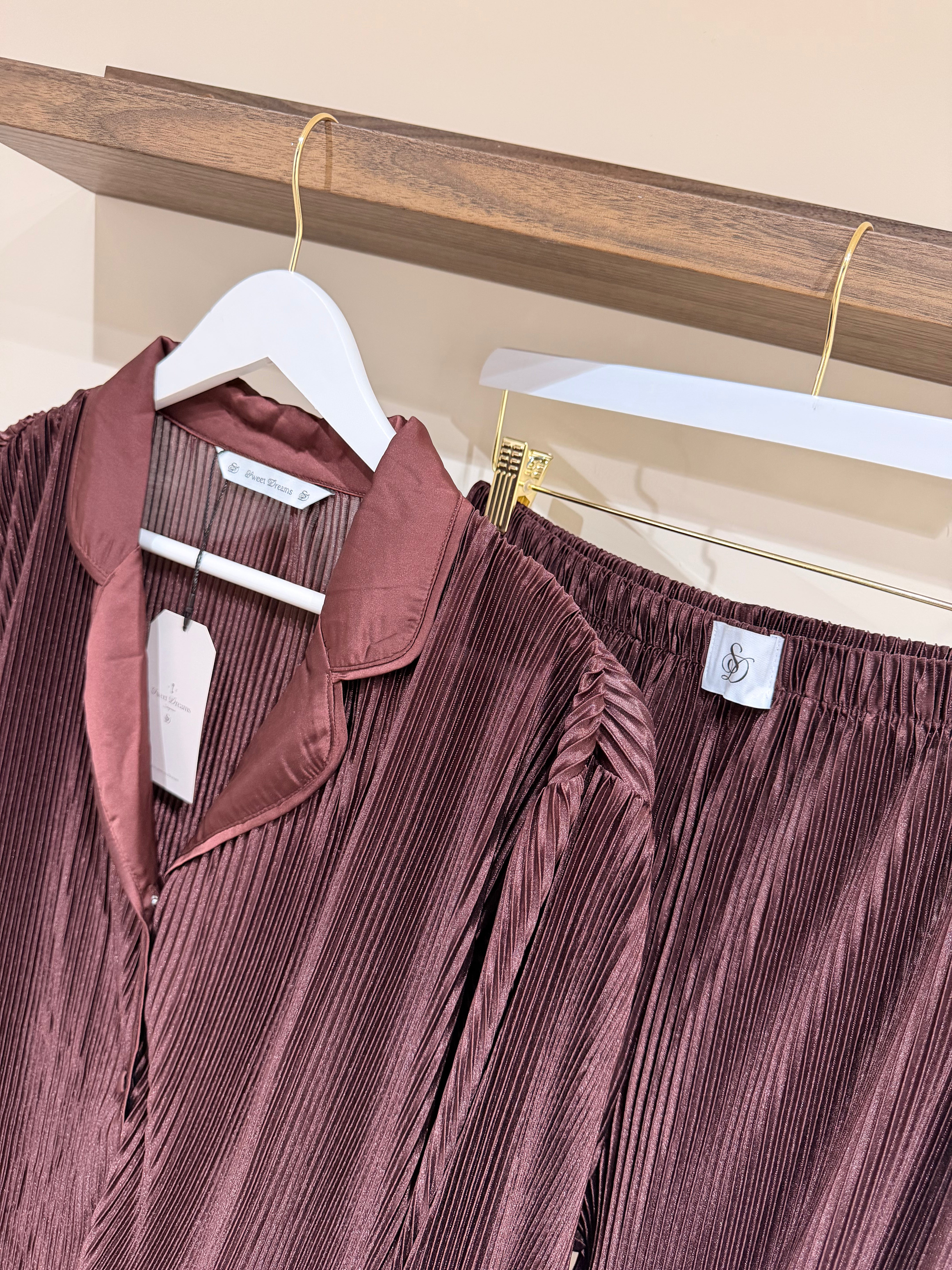 Burgundy pleated shirt and pants on pyjamas set with tags against a wooden shelf.