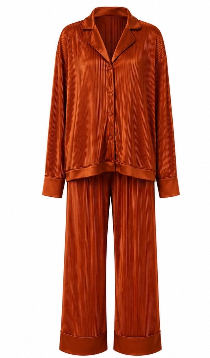 A two-piece matching pajama set in a rich rust-orange color, featuring a long-sleeve button-up shirt and wide-leg trousers, both with a vertical pleated texture, shown against a plain white background.