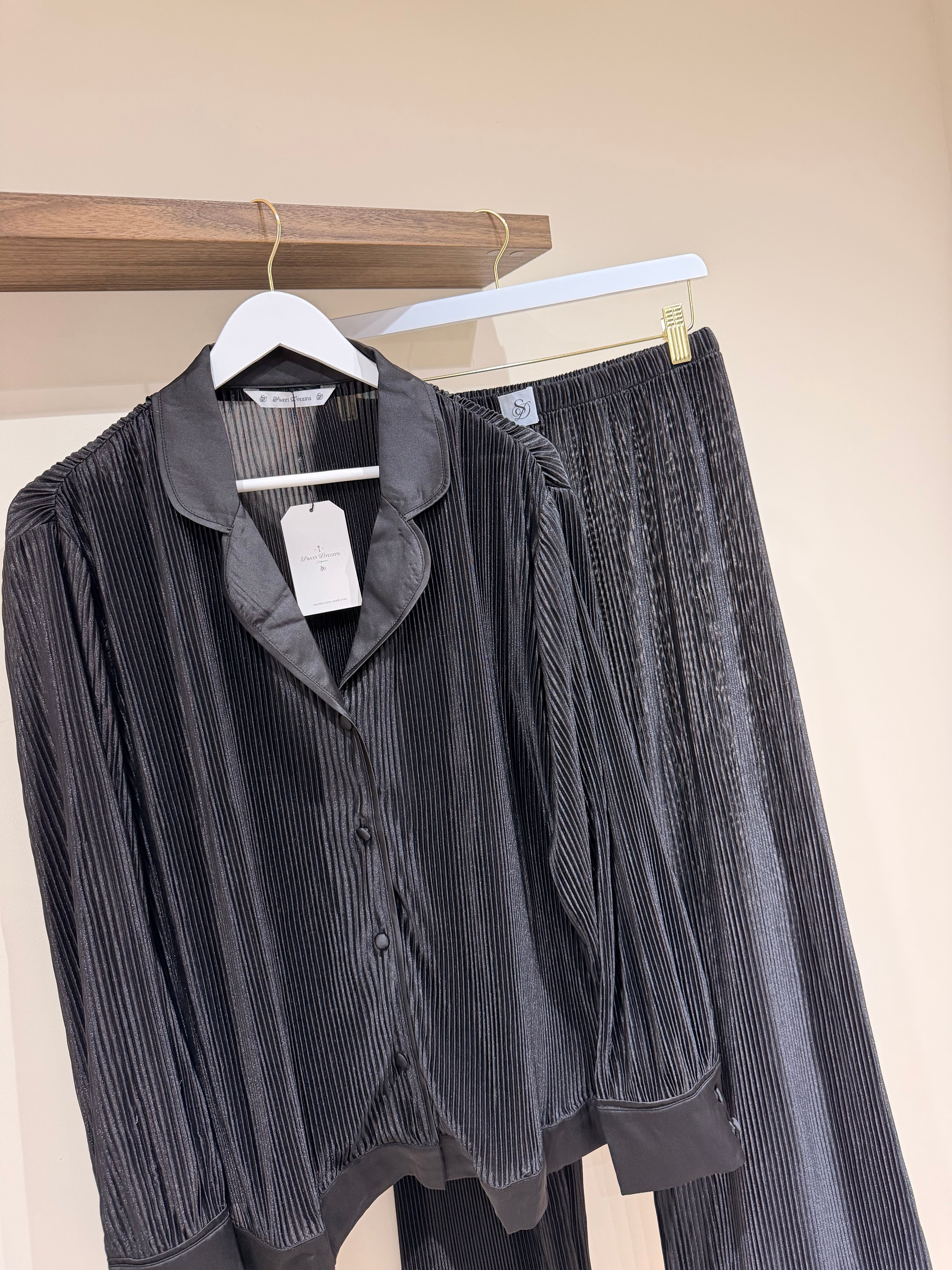 Hanging black pyjamas set  on a wooden rack against a beige wall.