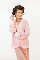Woman in a pink pajama set with curlers in her hair on a white background in content studio