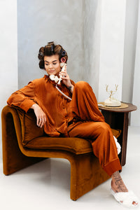 Person in a vintage-style outfit sitting on a brown chair, holding a white phone.