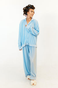 Woman wearing a light blue plisse pyjama set with curlers on a white background