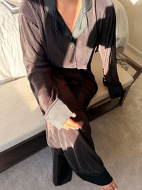 Person wearing a patterned shirt and black pants sitting on a couch.