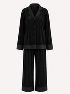 A two-piece black pajama set featuring a long-sleeve button-front shirt with a satin-like finish and wide-leg pants, shown against a plain light background.