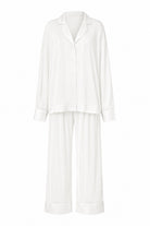 A two-piece white pajama set consisting of a long-sleeve button-front top with a collar and matching wide-leg pants, shown on a plain white background.