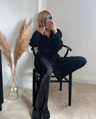 A person sitting on a chair wearing a black pyjama with satin lapels and cuffs, featuring a relaxed fit.